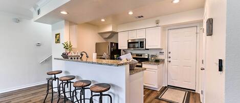 Una cocina moderna con armarios blancos, encimera de granito y refrigerador de acero inoxidable.