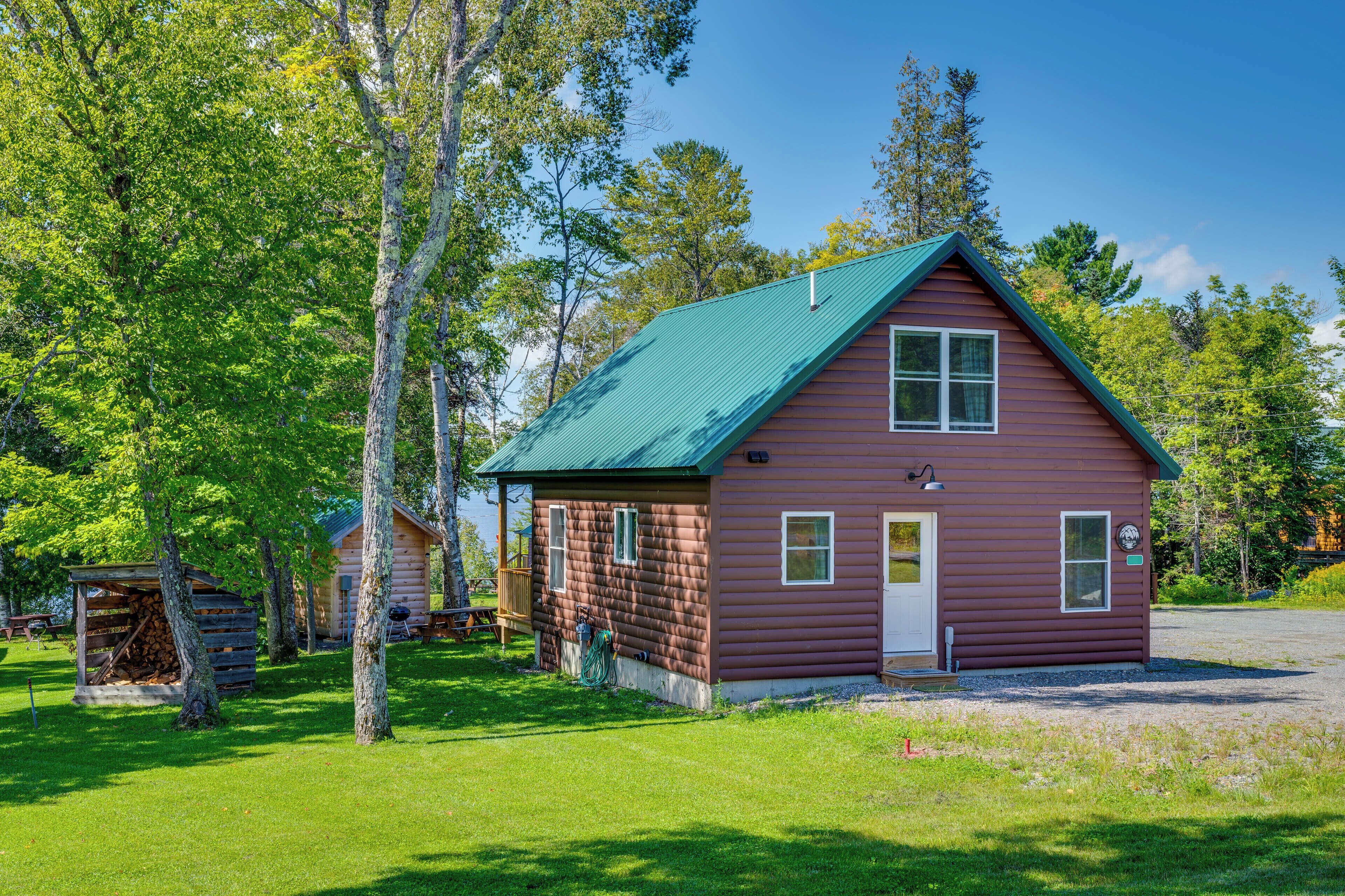 A log cabin with a green roof, surrounded by trees and a picnic table.