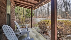 Une cabane en bois avec une véranda, deux fauteuils Adirondack et une vue sur une zone boisée.