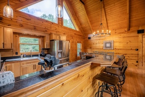 A wooden cabin interior with a kitchen, dining area, and large windows.