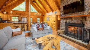 L’intérieur d’une cabane en rondins, avec une cheminée en pierre, des poutres en bois au plafond, un canapé et un coin repas.