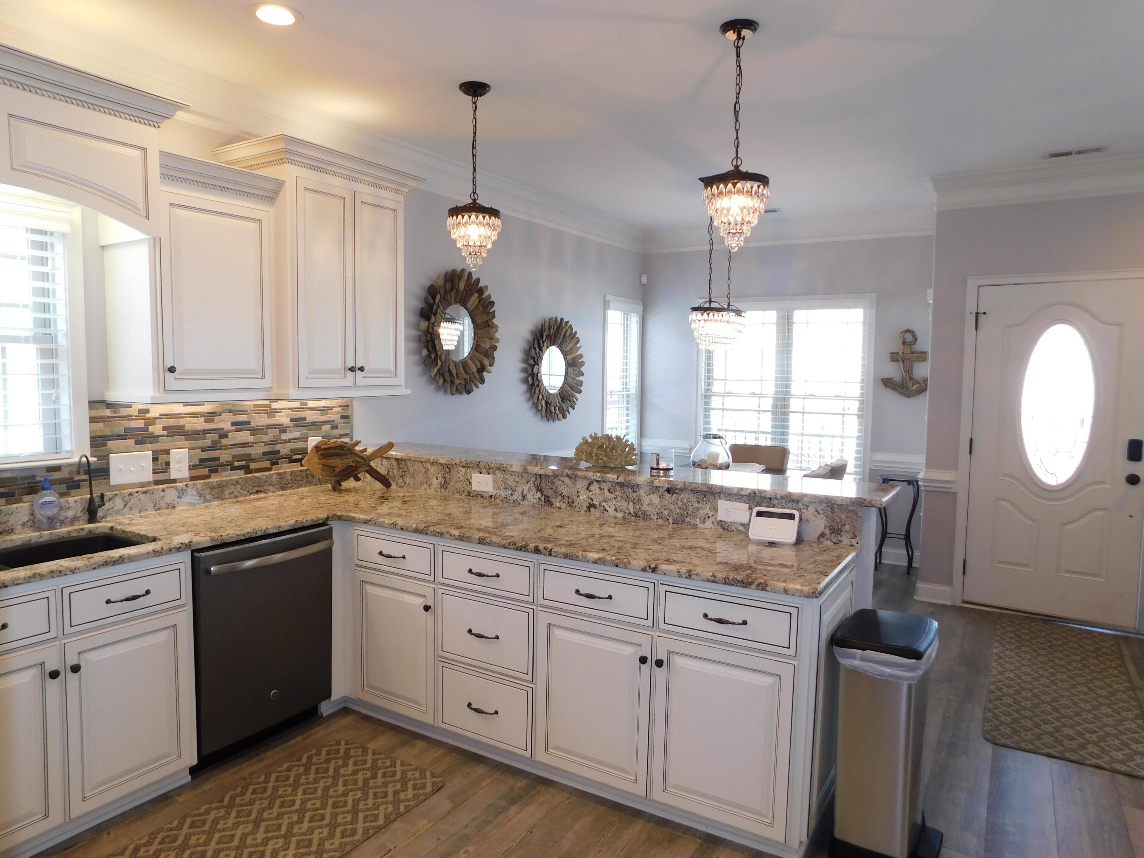 A kitchen with white cabinetry, granite countertops, a dishwasher, and a large island with a built-in oven.