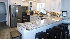 Una cocina moderna con armarios blancos, electrodomésticos de acero inoxidable, encimera de granito y una lámpara de araña.