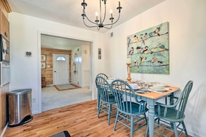 A dining area with a wooden table and four chairs, a chandelier, and a bird painting on the wall. - Berkeley Springs Vacation Home w/ Fire Pit! (Berkeley Springs)