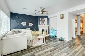 Relax in this stylish living room with a sofa set against a geometric-patterned accent wall, a dining table, and a cozy rug.