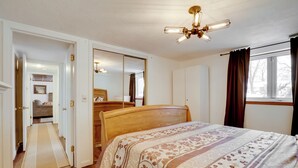 A bedroom with a wooden bed, a large mirror, a ceiling light fixture, and a window with curtains. - Pet-Friendly Minneapolis Apt Near Shops & Dining! (Minneapolis)