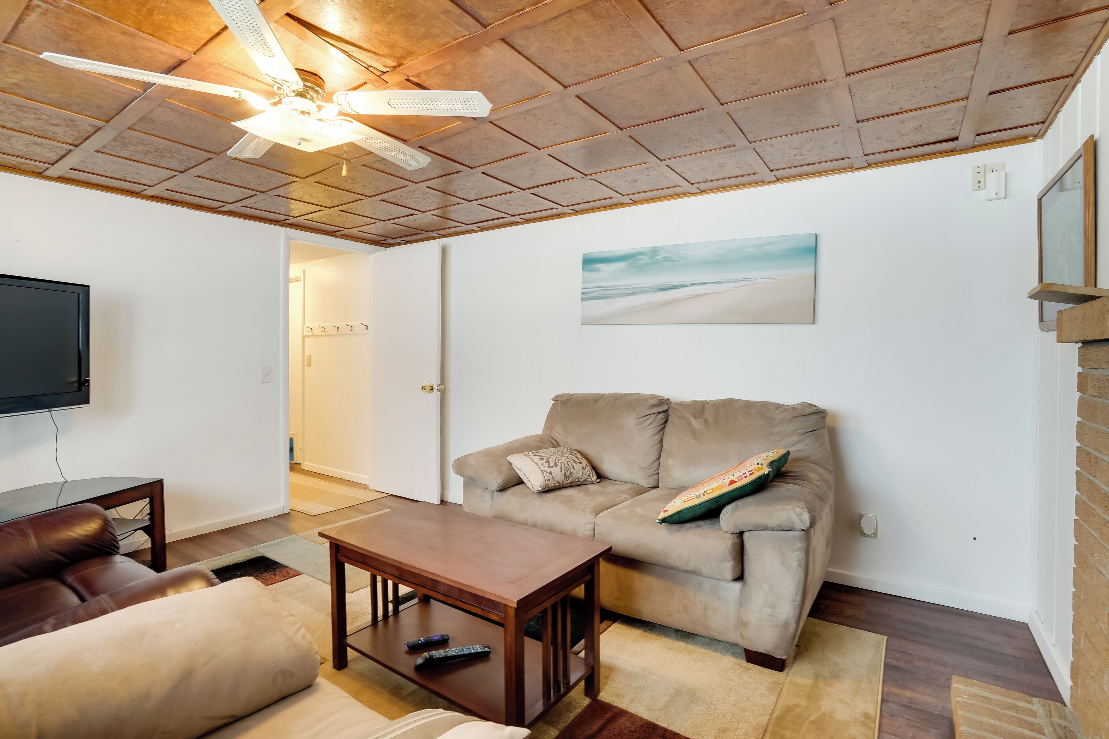 A living room with a ceiling fan, a flat-screen TV, a beige sofa, a wooden coffee table, and a painting on the wall.