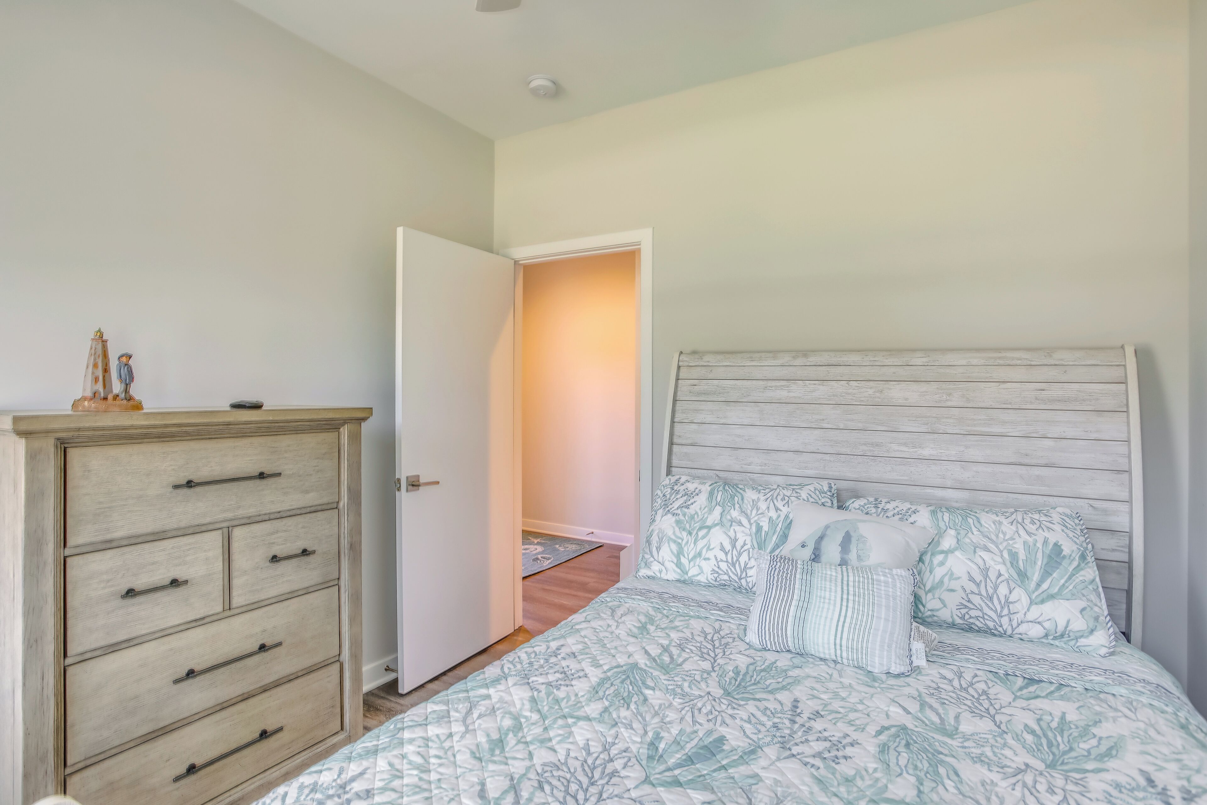 A bedroom with a bed, a wooden dresser, and an open door leading to another room.