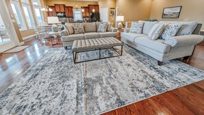 A spacious living room with a large sectional sofa, a matching ottoman, and a patterned rug.