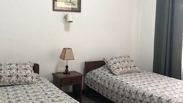 A room with two single beds, a nightstand with a lamp, a framed picture on the wall, and a window with curtains.