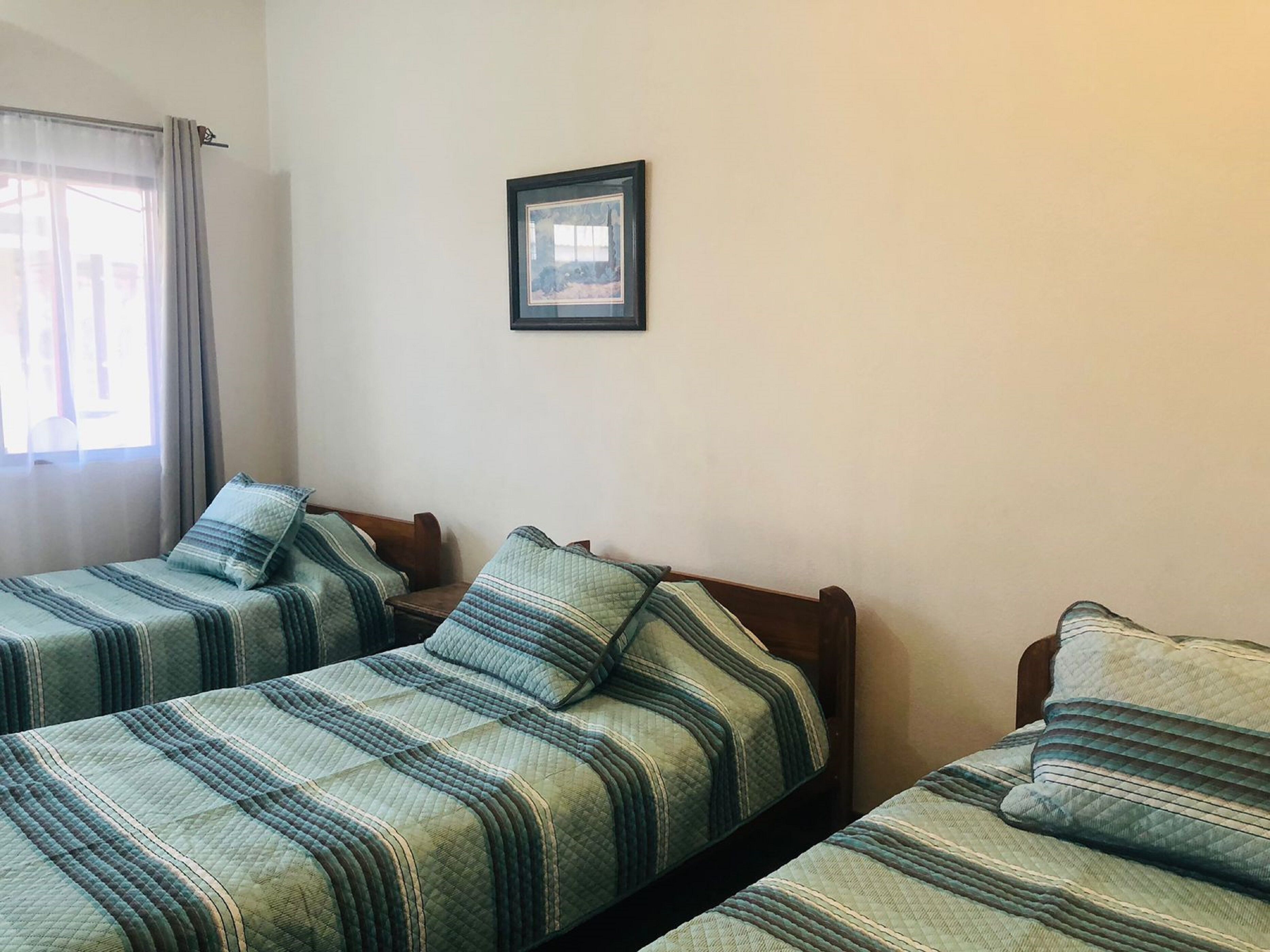Een kamer met twee eenpersoonsbedden, elk met een gestreept dekbedovertrek en passend kussen. Daarboven hangt een lijst met een afbeelding aan de muur.