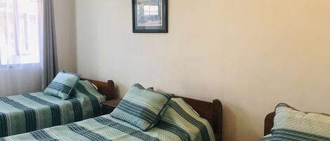 Een kamer met twee eenpersoonsbedden, elk met een gestreept dekbedovertrek en passend kussen. Daarboven hangt een lijst met een afbeelding aan de muur.