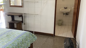 A bedroom with a bed, a desk, a wall-mounted drying rack, a mirror, a sink, and a fan.