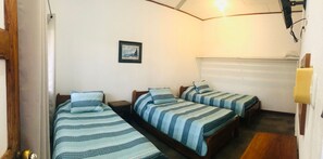 Una habitación con tres camas individuales, una mesita, un cuadro en la pared y una ventana con persianas.