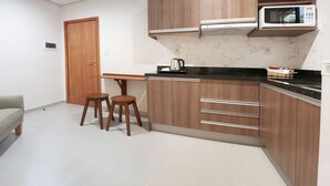 Cocina compacta con armarios de madera, una encimera, microondas y dos taburetes.
