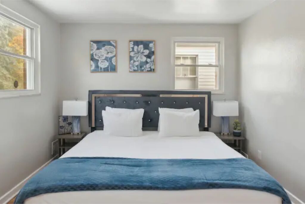 Une chambre à coucher comprenant un lit, deux lampes fixées au mur, une fenêtre et deux tableaux représentant des motifs floraux.
