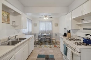A compact kitchen with white cabinets, a gas stove, a sink, and a dining area with a table and chairs.