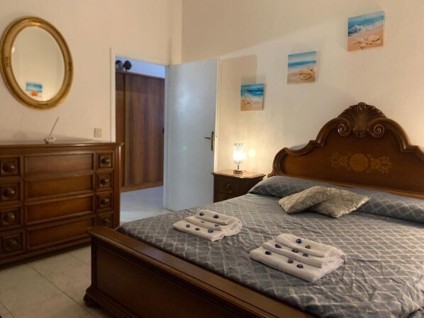 Ein Hotelzimmer mit einem hölzernen Bett, einem Schminktisch, einem Spiegel und einem Nachttisch mit Lampe.