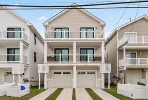 A two-story residential building with a central garage, balconies, and a clear sky.