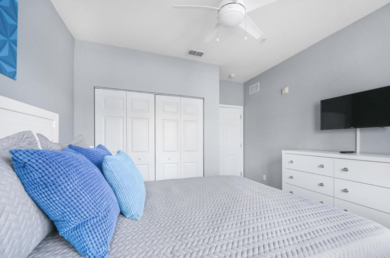 A bedroom with a bed, white dresser, TV, and a ceiling fan.