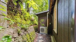 A narrow stone pathway leading to a building with a moss-covered wall and an air conditioning unit.