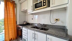 Una cocina con armarios blancos, encimera de granito, estufa, microondas y una ventana con cortinas anaranjadas.