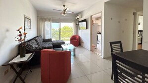 Una sala de estar con un sofá, una silla roja, una mesa de comedor y un ventilador de techo.