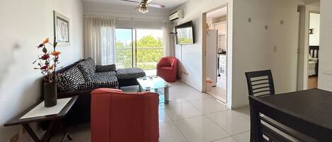 A living room with a sofa, a red chair, a dining table, and a ceiling fan.