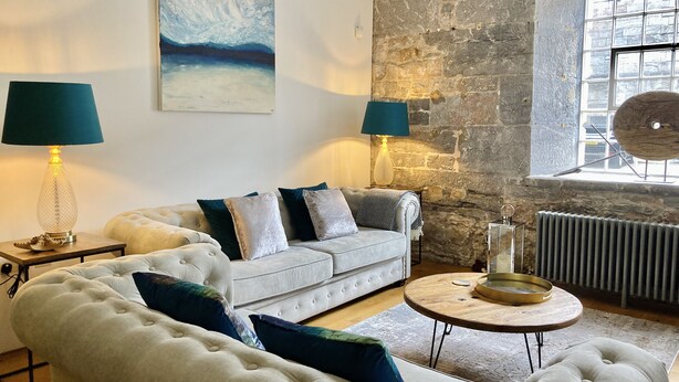 Una sala de estar con pared de piedra, un sofá blanco, una mesa de centro redonda de madera y dos lámparas.