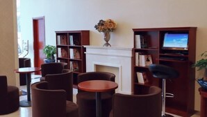 A lobby with round tables and sofas, a fireplace, and bookshelves with a television. - Greentree Inn Xuzhou Kuangda Huaita East Gate Express Hotel (Xuzhou)