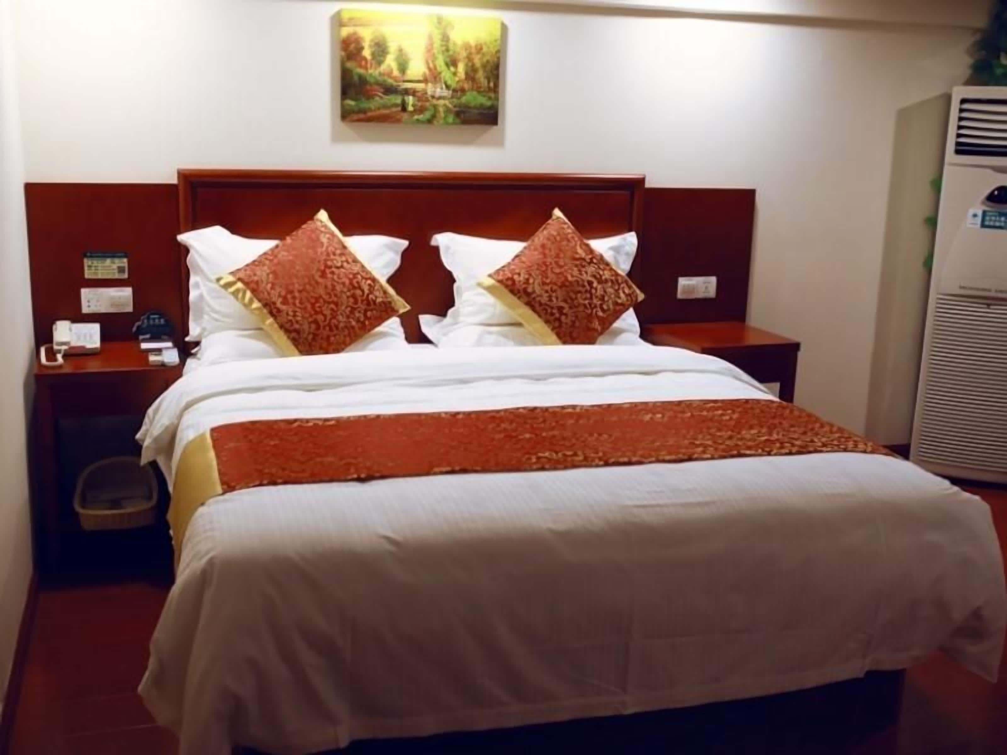 A hotel room with a bed, a nightstand, a wall-mounted phone, and a painting above the bed.