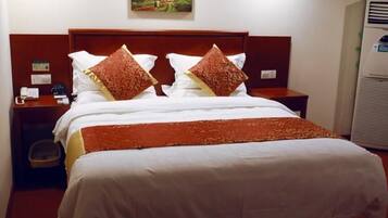 A hotel room with a bed, a nightstand, a wall-mounted phone, and a painting above the bed.
