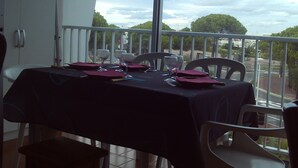 A balcony table set with a tablecloth, chairs, and wine glasses, overlooking a street and trees.
