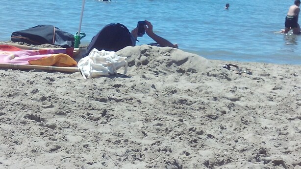 A sandy beach with a striped umbrella and a bag on the sand.