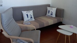 A modern living room with a sofa, armchair, and small table. There is a painting on the wall and a clock.