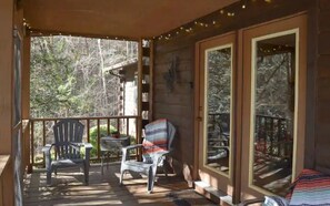 A wooden cabin with a porch featuring two Adirondack chairs and a small table.