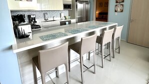 A modern kitchen with a central island, stainless steel appliances, and a seating area with bar stools. - Waykiri Unit C-12 Luxurious New Apartment (Noord)