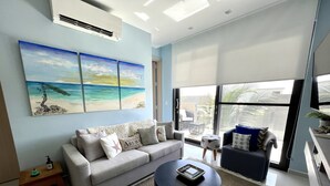 A modern living room with a sofa, a coffee table, and a painting of a beach scene. - Waykiri Unit C-12 Luxurious New Apartment (Noord)