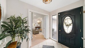 Un vestíbulo moderno con una puerta oscura, una planta en maceta y una lámpara.