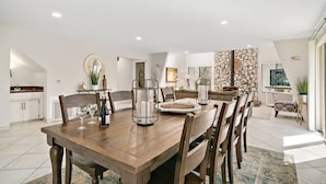 Un comedor con una mesa de madera, sillas y candelabros. Se observa una pared de piedra y una ventana al fondo.