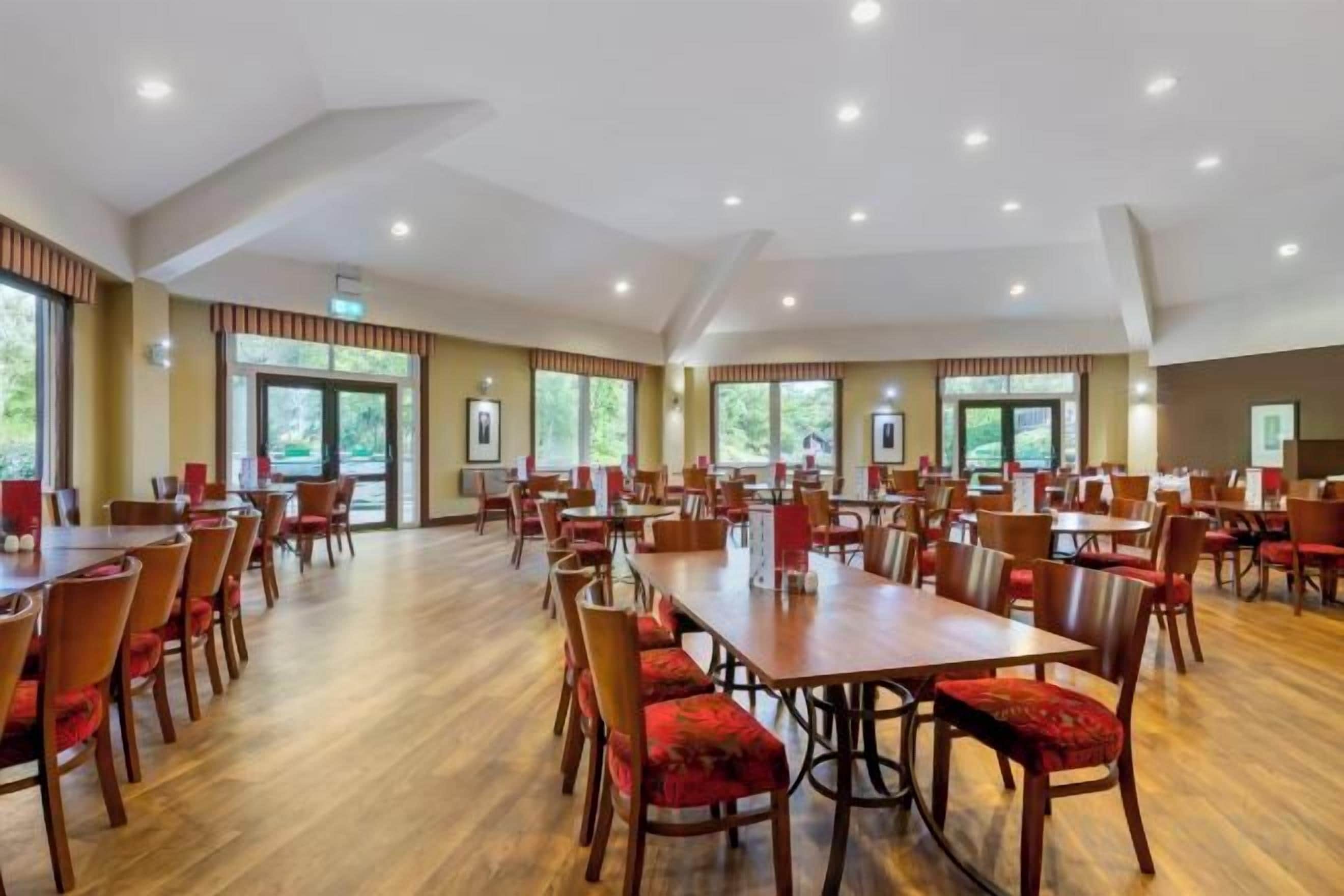 A spacious dining area with multiple tables and chairs, large windows, and a high ceiling.