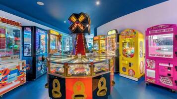 A brightly lit arcade with various gaming machines, including claw machines and racing games.