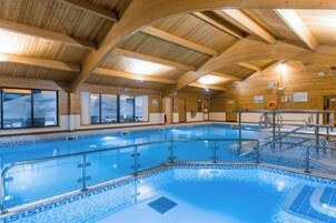 Piscina interna com vigas de madeira, guarda-corpo de vidro transparente e piso cerâmico.