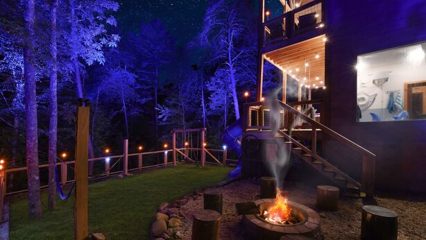 A modern outdoor area with a fire pit, wooden benches, and a staircase leading to a second level.