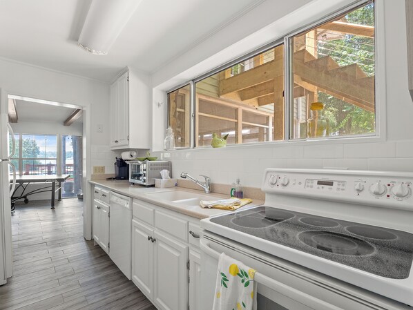 A kitchen with white cabinets, a stove, and a window overlooking a wooden deck. - Sheltered Cove - Family-friendly with lots of options! (Jasper)