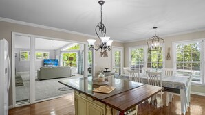 Una cocina amplia con una isla de madera, muebles blancos y un comedor con sillas y una mesa blancos.
