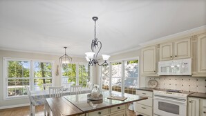 Una cocina con una isla central, armarios blancos y un amplio ventanal con vistas a la vegetación.