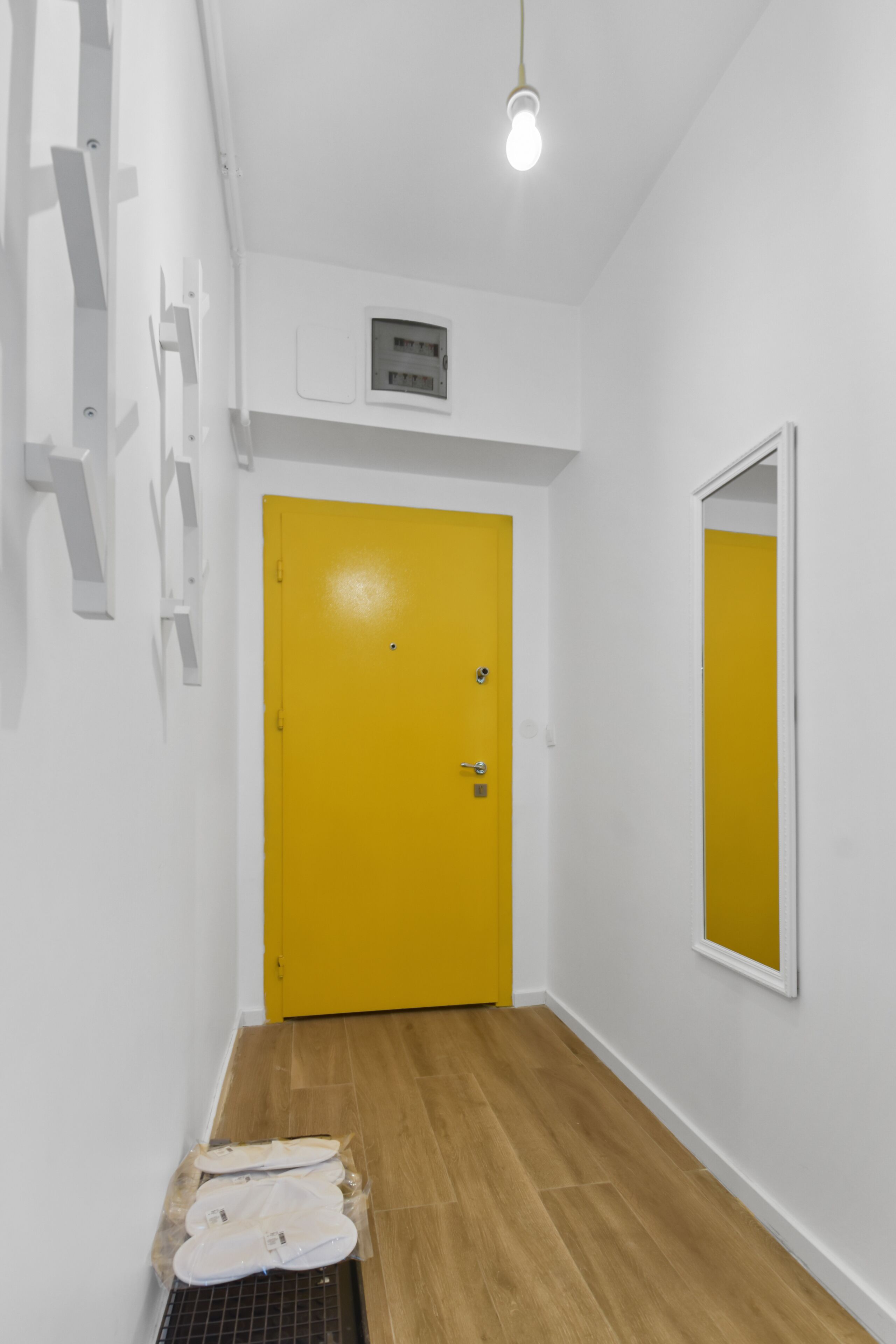 Un couloir avec une porte jaune, des murs blancs et un luminaire.