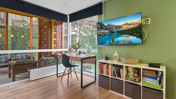Ein modernes Wohnzimmer mit großem Fenster, einem Schreibtisch, einer gemütlichen Sitzecke und einem Bücherregal mit Büchern und Puzzles.