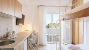 Une chambre d’hôtel moderne dotée d’un coin cuisine, d’un balcon avec vue et d’un lit agrémenté d’une serviette blanche soigneusement pliée.